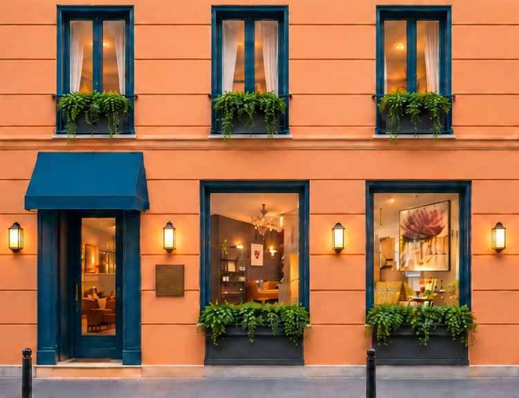 Façade d’un hôtel parisien aux murs orangés, fenêtres bleues fleuries et lanternes allumées